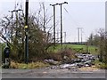 Footpath heading up a muddy track, past a field full of wooden pylons