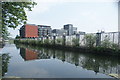 View of the fence on the edge of Fish Island and the Omega Works apartments on Roach Road reflected in the Hertford Union Canal