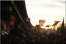 TQ2481 : View of flags against the setting sun in the Portobello Road Winter Festival from Acklam Road by Robert Lamb