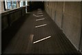 View of narrow beams of light shining through the slits in the side of the undercover walkway leading from the Barbican Estate