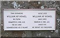 A memorial fastened to the church wall along side a very old grave stone.